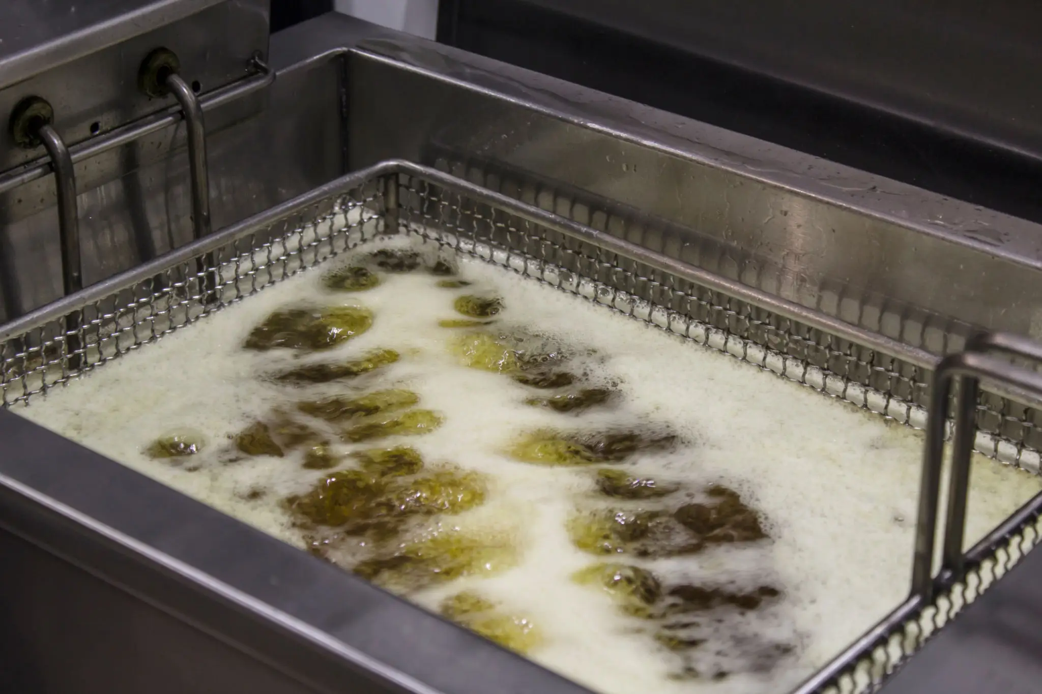Food frying in bubbling oil inside a deep fryer.