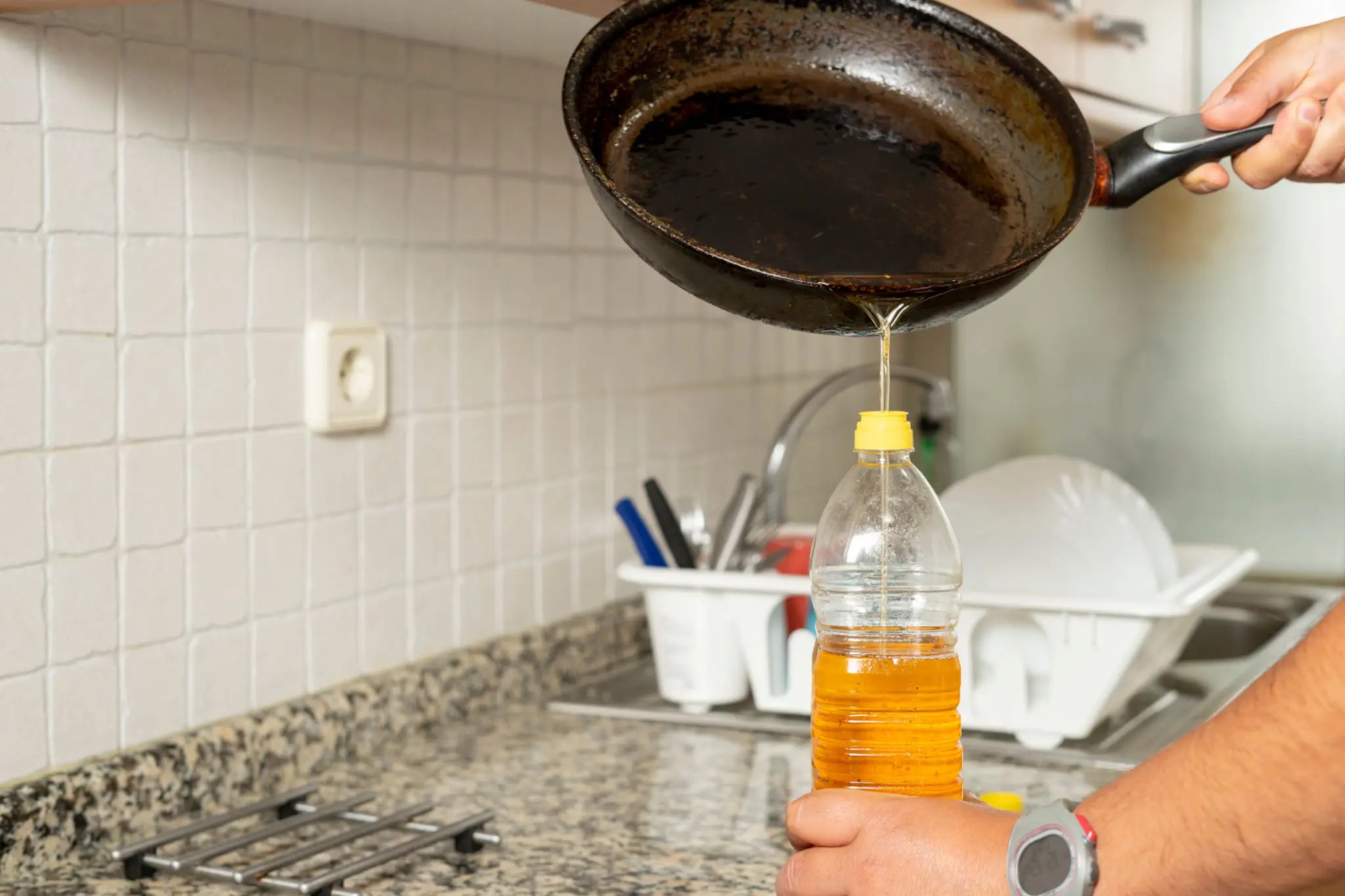 Pouring cooking oil from a pan into a bottle in a kitchen.